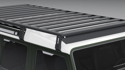 Detailansicht: Schwarze Montagehalterungen und Befestigungssystem des modularen Dachträgers an der Regenrinne eines Land Rover Defender.