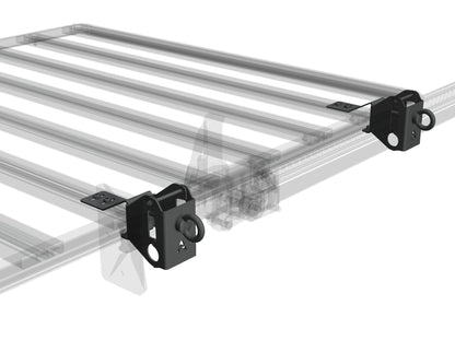 3D-Render einer Airholder Dachträger-Plattform mit zwei Zurrpunkten an den Außenecken: Die schwarz beschichteten Eckhalter werden am Außenprofil montiert und bieten jeweils eine massive Ringöse als sicheren Anschlagpunkt für Spanngurte, Seile oder Karabiner. Durch die kompakte Bauform bleibt die Ladefläche frei, während die Verzurrung direkt am Rahmen erfolgt. Position: Eckbereich der Plattform am Außenrahmen (vorn/hinten je nach Montage, links und rechts möglich).
