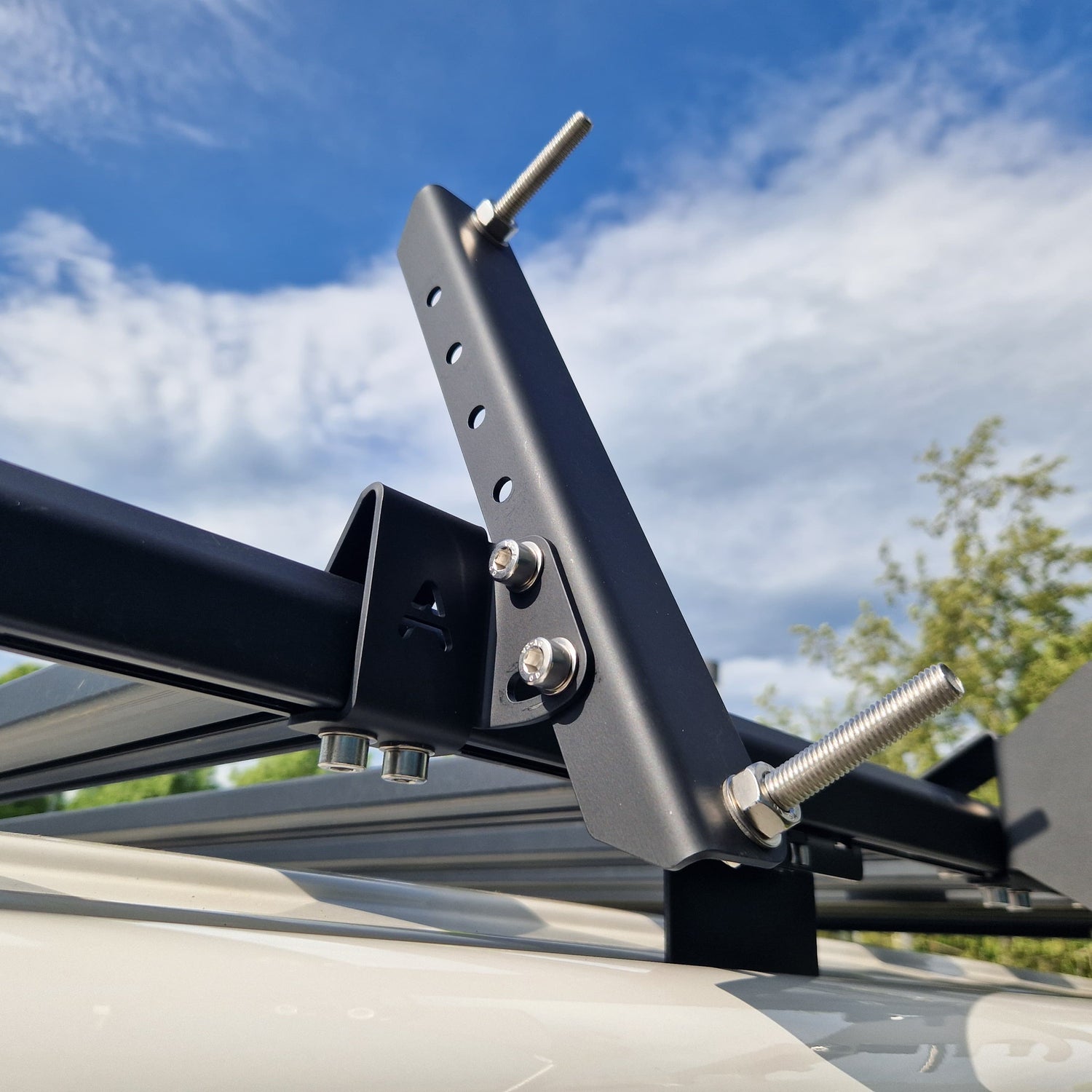 Reales Outdoor-Foto: montierte Airholder Universal-Seitenhalterung am Außenprofil des Dachträgers – robuste Metallkonsole mit verstellbarer Halteschiene (Lochraster), Edelstahl-Schrauben und zwei Gewindestiften zur Aufnahme und Fixierung von Bergungsboards/MAXTRAX.
